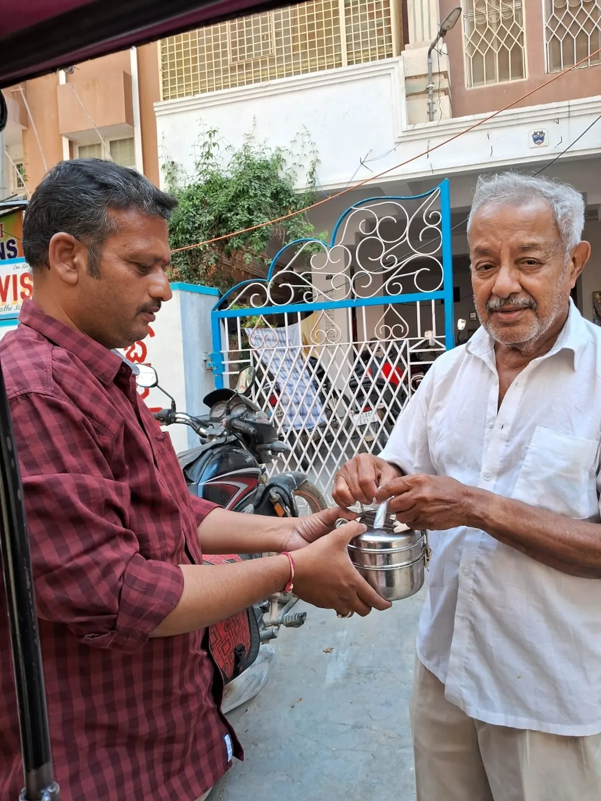 A volunteer handing a packed meal to an elderly man at his gate during the daily round