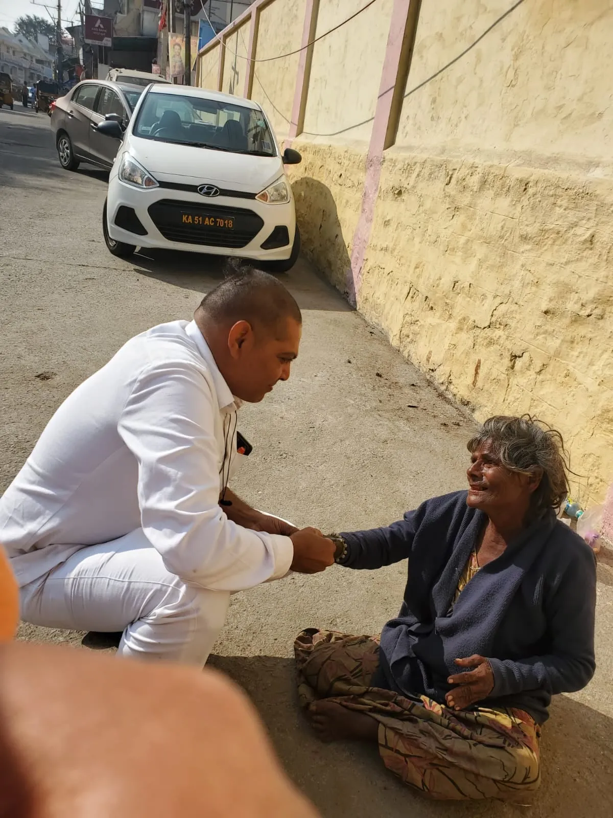 A volunteer kneeling in the street to sit with an elderly man during the daily round