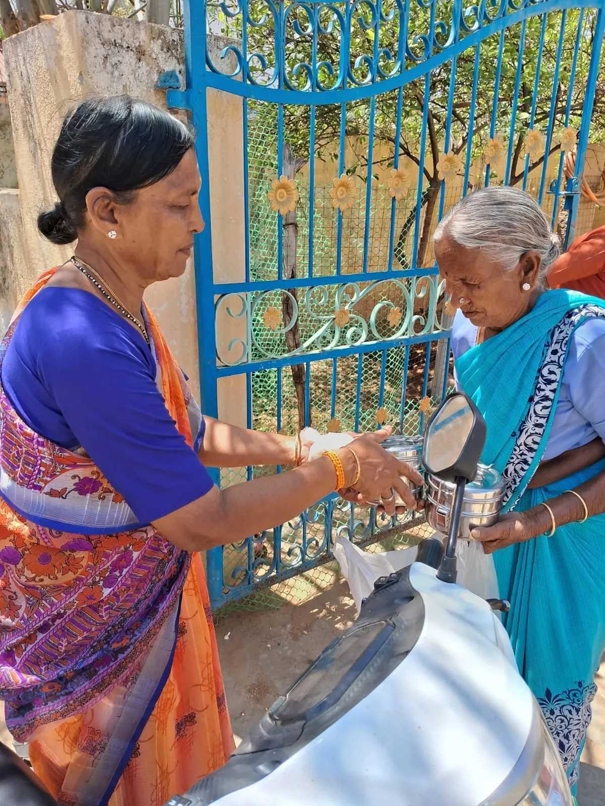 A water can being handed to an elderly woman at the Kuteer gate
